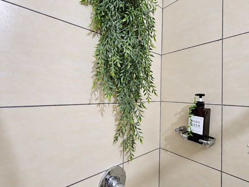 A close-up view of a shower enclosure featuring beige wall tiles, a chrome shower mixer, and a fixed soap dish.