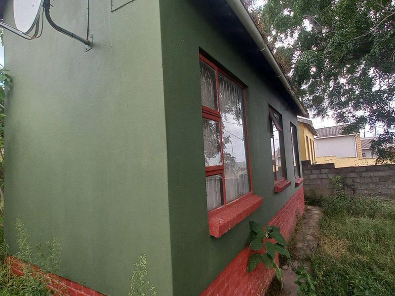 Side view of the property exterior featuring painted brick walls, window frames, and a satellite dish installation.