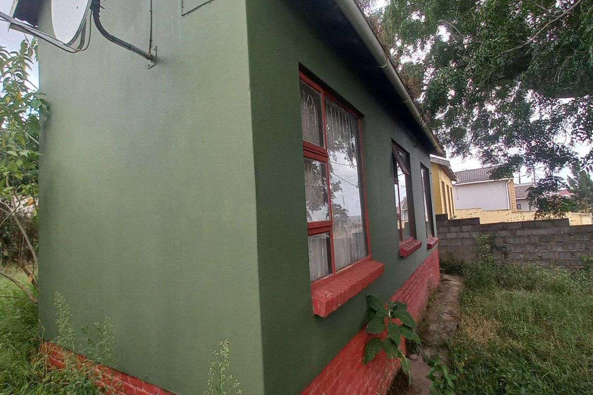 Side view of the property exterior featuring painted brick walls, window frames, and a satellite dish installation.
