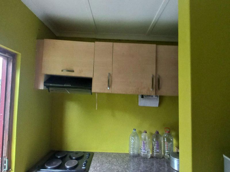 A compact kitchen area featuring built-in cabinetry, an electric hob, and an extractor fan, requiring cosmetic updates to the wall finishes.