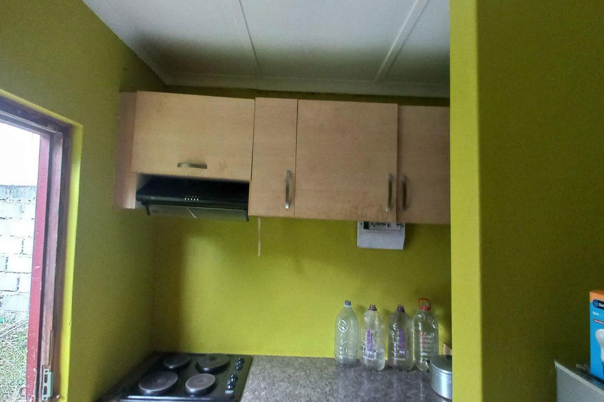 A compact kitchen area featuring built-in cabinetry, an electric hob, and an extractor fan, requiring cosmetic updates to the wall finishes.