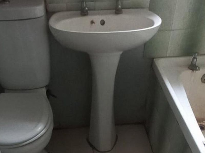 A dated bathroom featuring a standard pedestal basin, toilet, and bathtub with tiled wall finishes, requiring cosmetic updates and refurbishment.