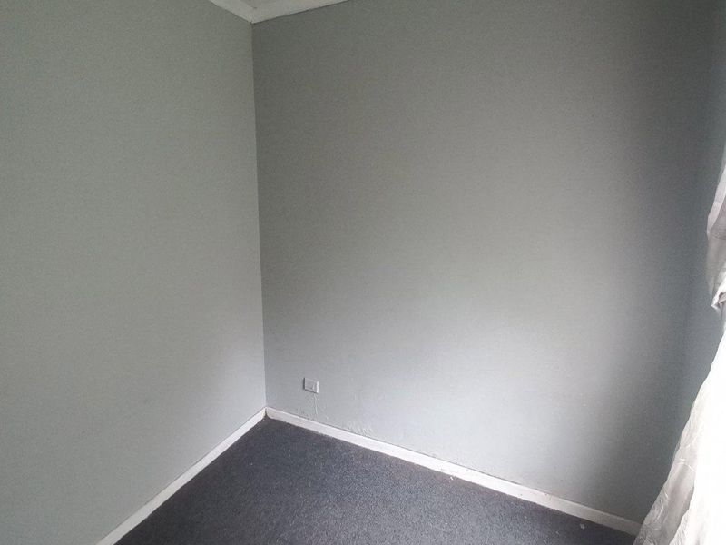 An empty bedroom featuring grey walls, carpet flooring, and standard electrical fixtures, ready for personalization or staging.