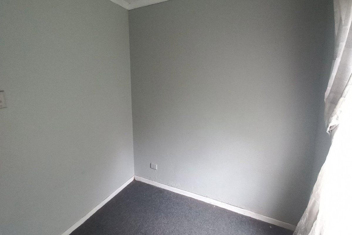An empty bedroom featuring grey walls, carpet flooring, and standard electrical fixtures, ready for personalization or staging.