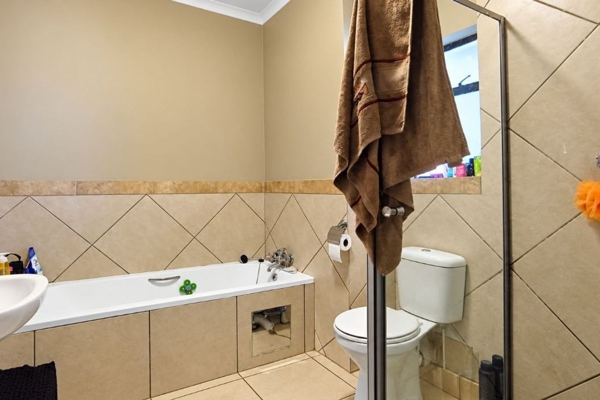 A functional bathroom featuring a bathtub, pedestal sink, and toilet with neutral wall and floor tiling.