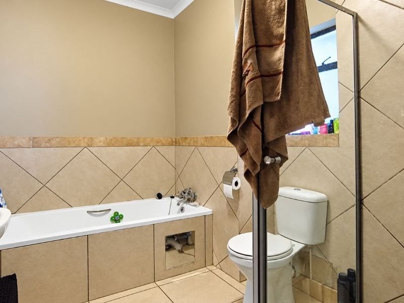 A functional bathroom featuring a bathtub, pedestal sink, and toilet with neutral wall and floor tiling.