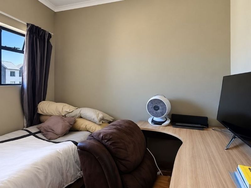 A functional bedroom featuring a built-in desk and an aluminium-framed window, providing a practical space for rest and study.