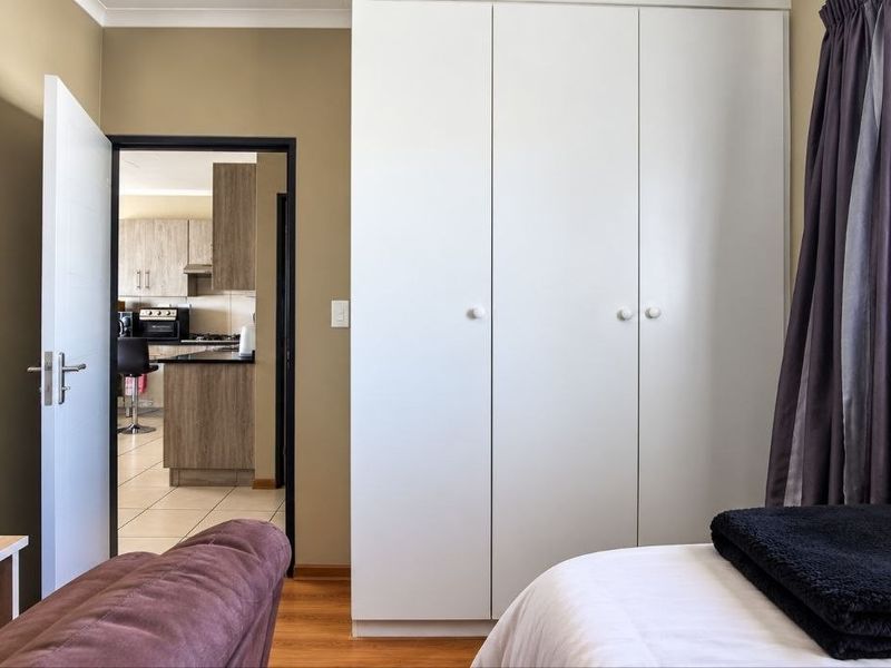 A well-maintained bedroom featuring built-in wardrobes, laminate flooring, and a view through the doorway into the adjacent kitchen area.