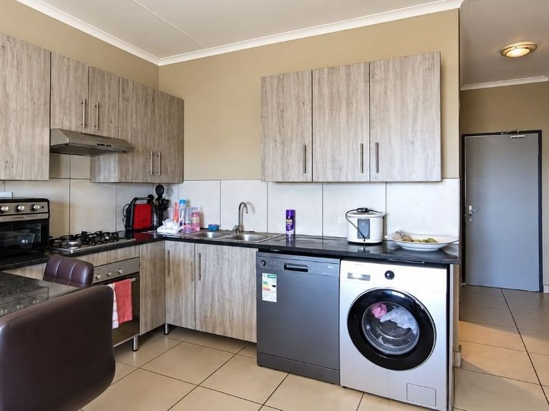 A functional kitchen featuring light wood-grain cabinetry, granite countertops, a gas hob, and integrated space for laundry appliances.