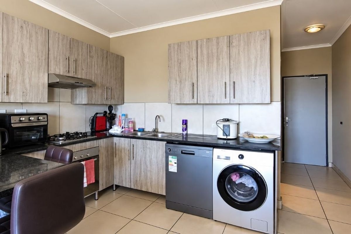 A functional kitchen featuring light wood-grain cabinetry, granite countertops, a gas hob, and integrated space for laundry appliances.