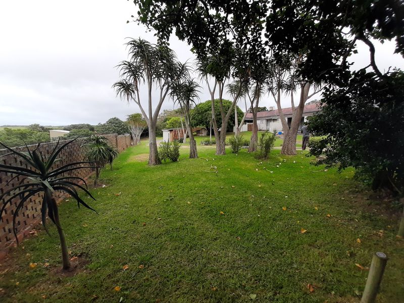 A spacious, well-established garden featuring mature trees, a manicured lawn, and a brick boundary wall, offering a peaceful outdoor setting.