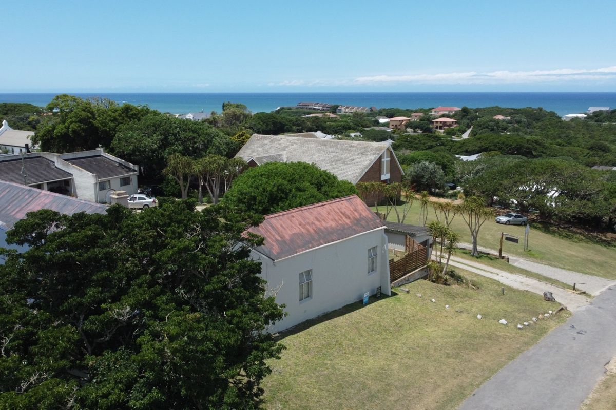 An aerial view of the property showing the surrounding coastal landscape, mature trees, and the building's pitched metal roof.