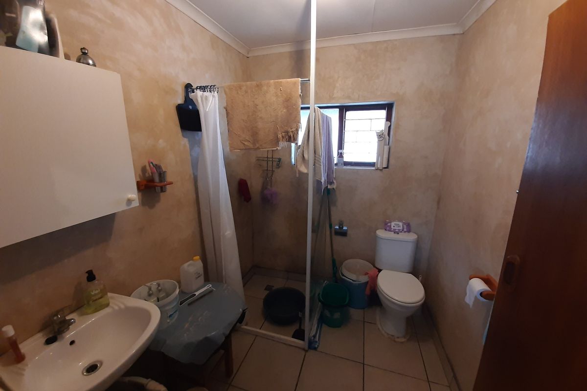 A functional bathroom featuring a pedestal basin, toilet, and shower enclosure with tiled flooring and textured wall finishes.