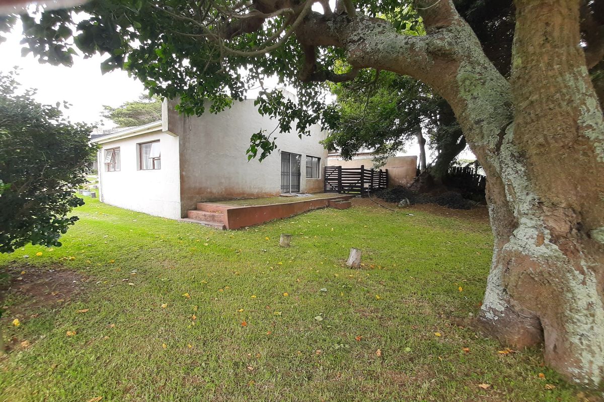 Rear view of the townhouse featuring a small concrete patio, security gate, and established garden area with mature trees.