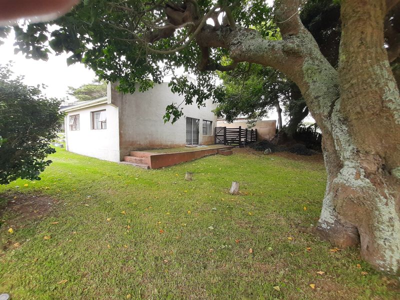 Rear view of the townhouse featuring a small concrete patio, security gate, and established garden area with mature trees.