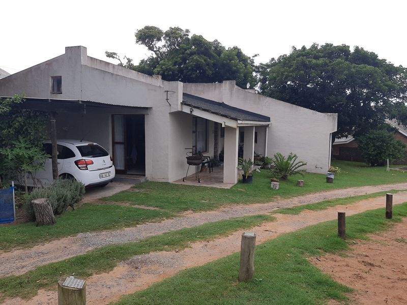 Front elevation of a townhouse featuring a covered carport, concrete patio area, and a simple stucco facade with a pitched roof design.