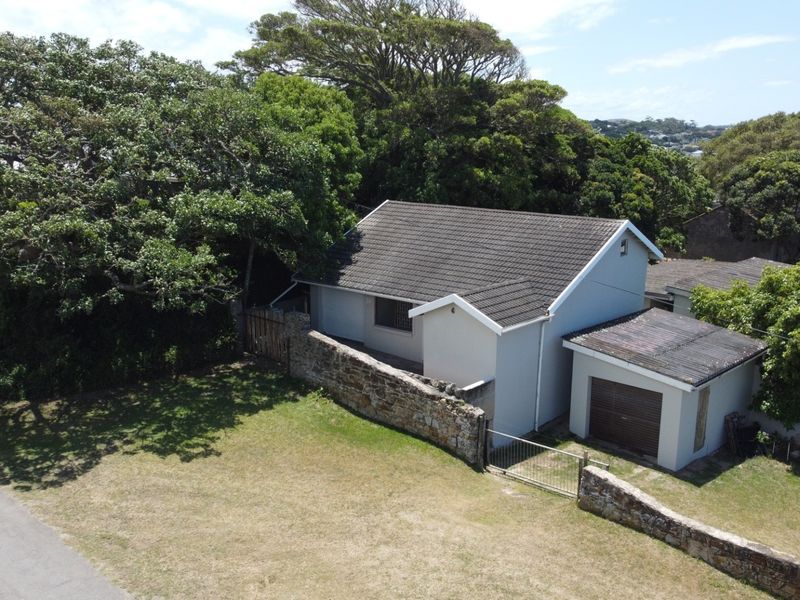 Aerial view of the townhouse property featuring a tiled roof, stone boundary wall, and attached garage set within a landscaped garden area.