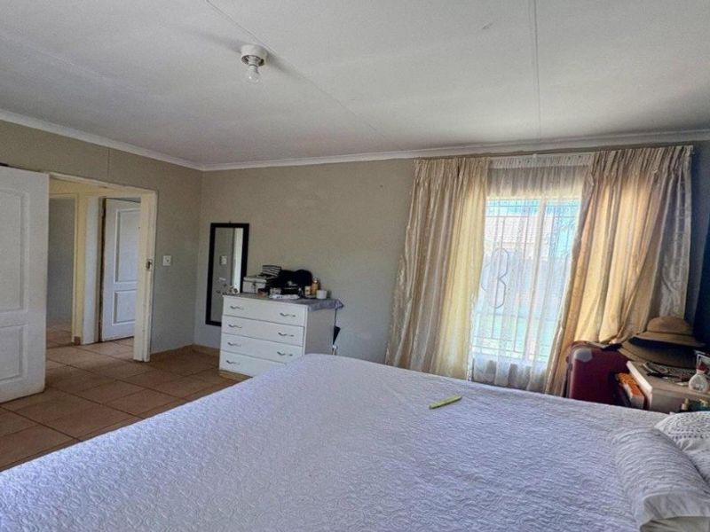 A bedroom featuring tiled flooring, coved ceilings, and a window fitted with security bars, providing access to an adjoining hallway.