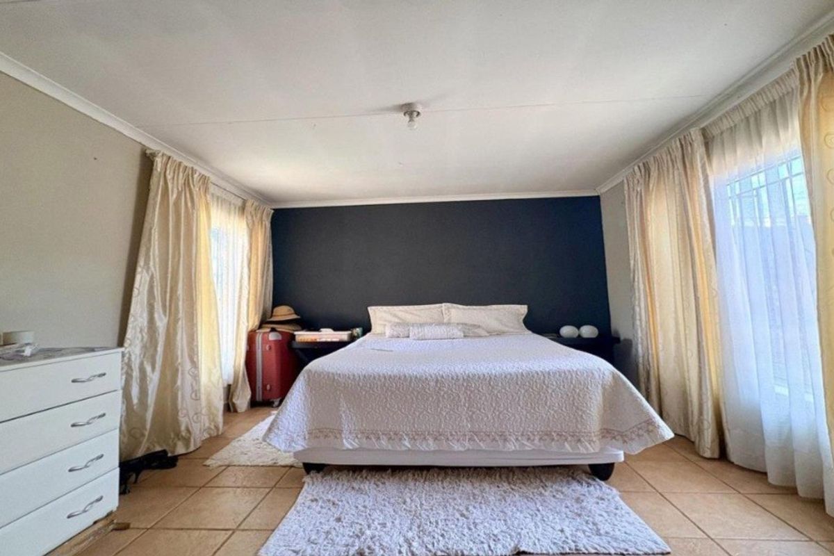 A spacious bedroom featuring tiled flooring, a dark accent wall, and dual windows with curtain treatments.