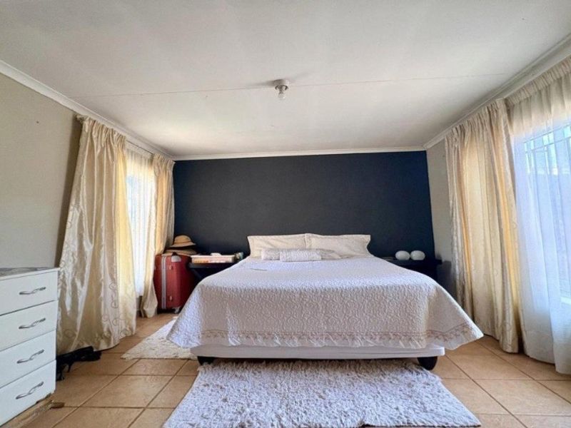 A spacious bedroom featuring tiled flooring, a dark accent wall, and dual windows with curtain treatments.