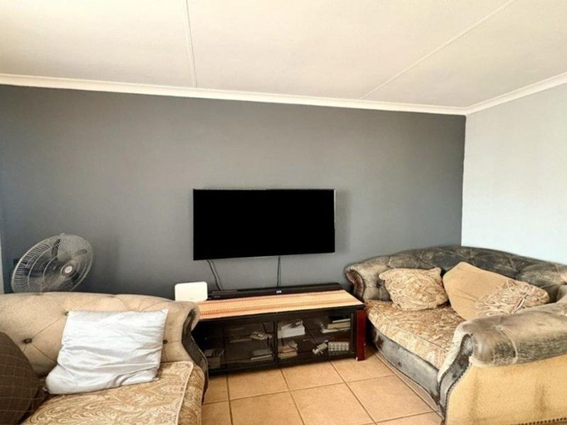 A living room featuring tiled flooring and a coved ceiling, with a neutral color palette and a dedicated wall-mounted television area.