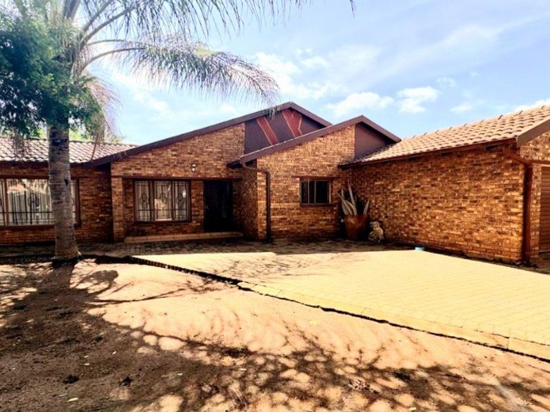 Front view of a single-story face-brick house featuring a tiled roof, paved driveway, and an attached garage.