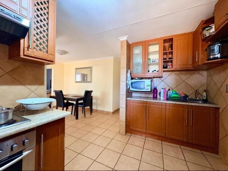 Open plan kitchen and dining area featuring wooden cabinetry, tiled flooring, and built-in appliances, offering a functional layout for daily living.