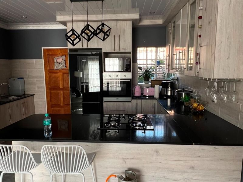 Modern kitchen featuring light wood-grain cabinetry, black granite countertops, a built-in gas hob, oven, and microwave, complemented by stylish pendant lighting.