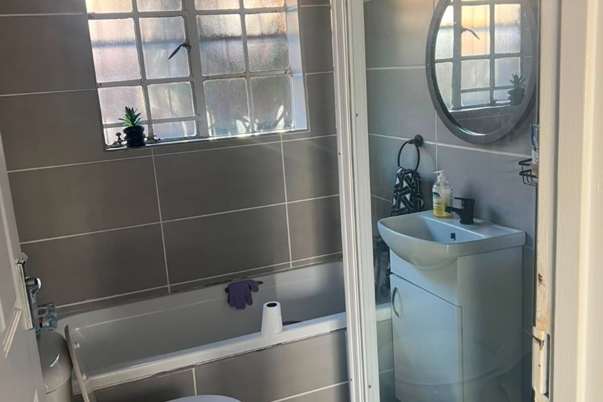 Compact bathroom featuring a bathtub, separate shower enclosure, vanity basin, and toilet with grey wall tiling.