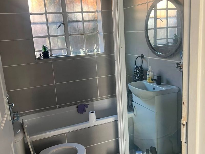 Compact bathroom featuring a bathtub, separate shower enclosure, vanity basin, and toilet with grey wall tiling.
