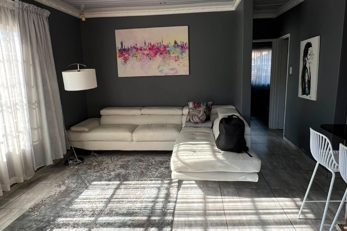 A well-maintained living room featuring large format floor tiles, a white tongue and groove ceiling with decorative cornicing, and recessed lighting.
