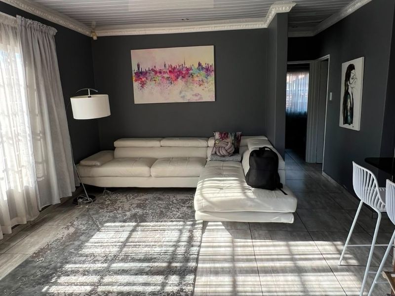 A well-maintained living room featuring large format floor tiles, a white tongue and groove ceiling with decorative cornicing, and recessed lighting.