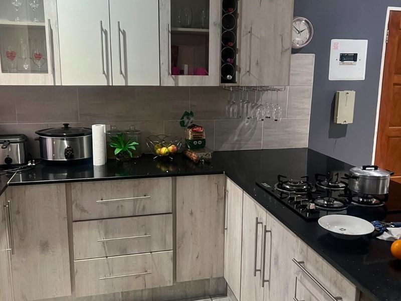 Modern kitchen featuring light wood-grain cabinetry, black granite countertops, a built-in gas hob, and neutral tiled flooring with a contemporary backsplash.