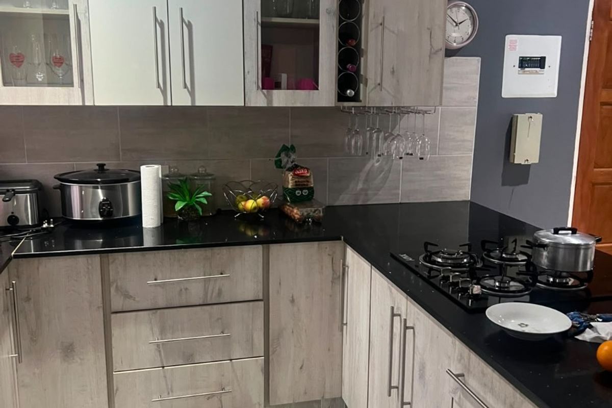 Modern kitchen featuring light wood-grain cabinetry, black granite countertops, a built-in gas hob, and neutral tiled flooring with a contemporary backsplash.