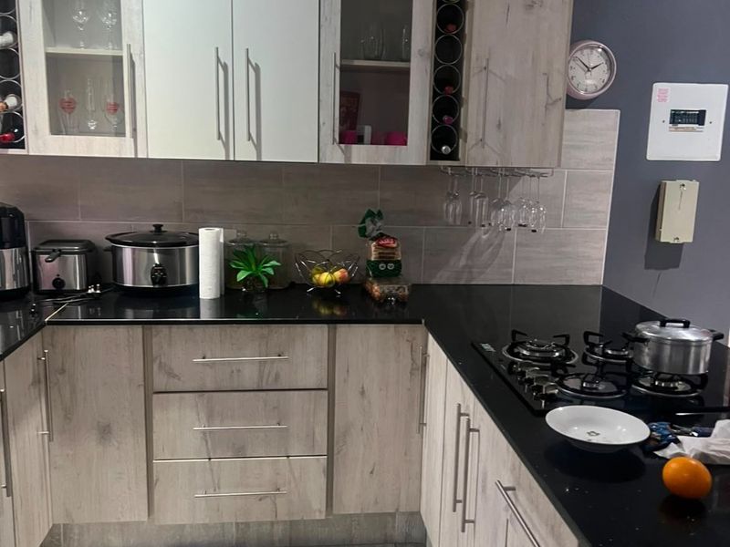 A modern kitchen featuring light wood-grain cabinetry, black granite countertops, a gas hob, and integrated wine storage with neutral tiled flooring.