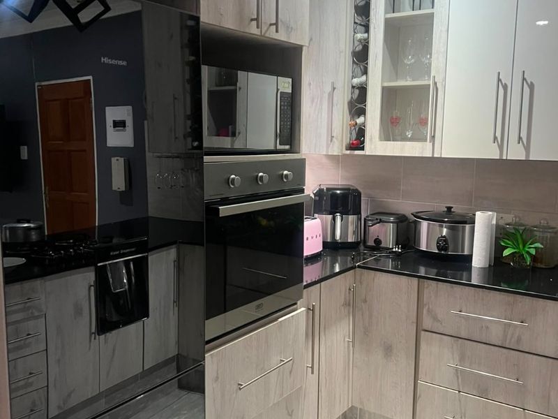 Modern kitchen featuring light wood-grain cabinetry, black granite countertops, built-in oven, microwave, and integrated hob with contemporary tiled flooring.