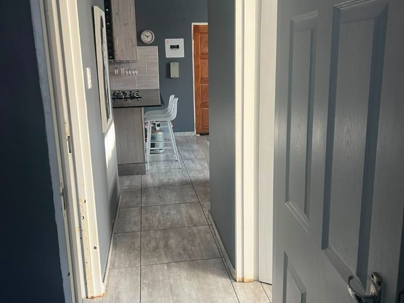 A view through a hallway leading into a kitchen area featuring tiled floors, built-in cabinetry, and a gas hob.