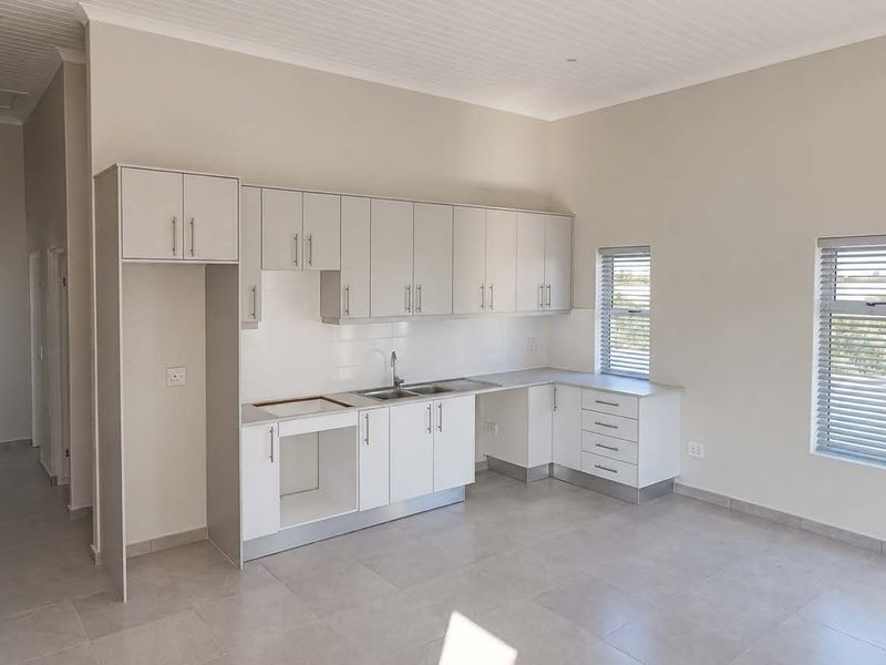 A clean, modern, and empty kitchen featuring neutral cabinetry, tiled floors, and ample natural light from the windows.