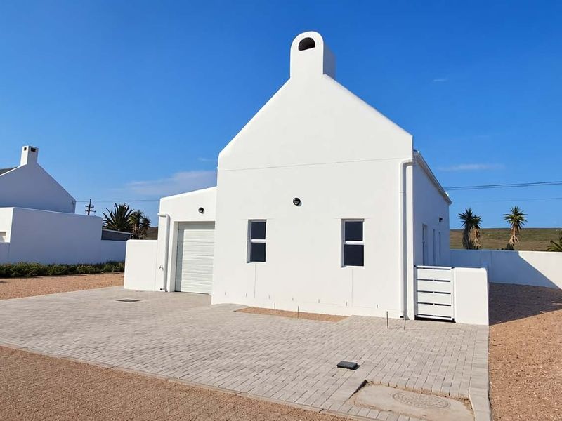 A well-maintained white house featuring a classic gable roof, chimney, paved driveway, and a secure garage entrance.