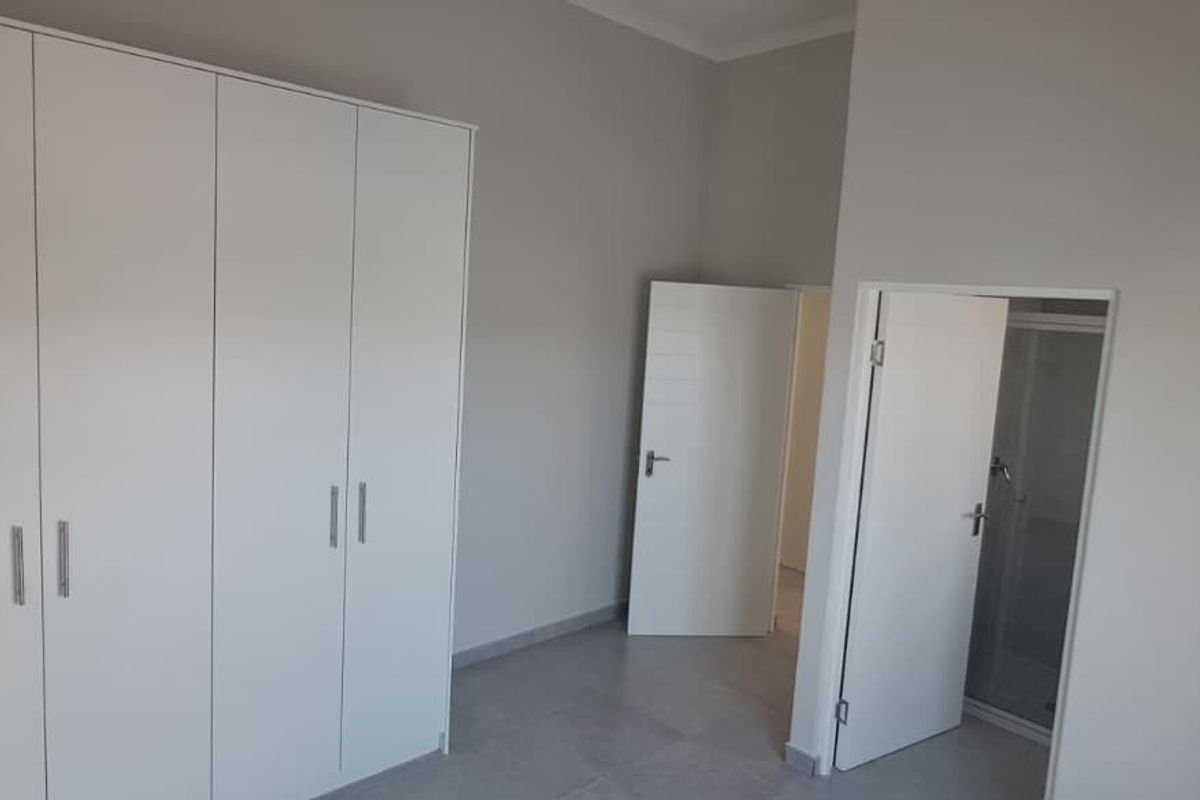 A clean, neutral bedroom featuring built-in cupboards, tiled flooring, and direct access to an en-suite bathroom.