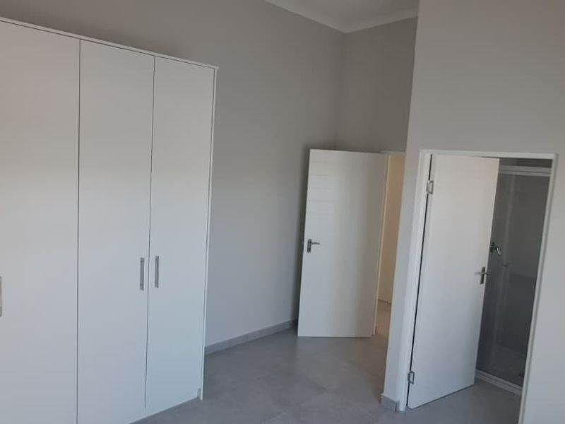 A clean, neutral bedroom featuring built-in cupboards, tiled flooring, and direct access to an en-suite bathroom.