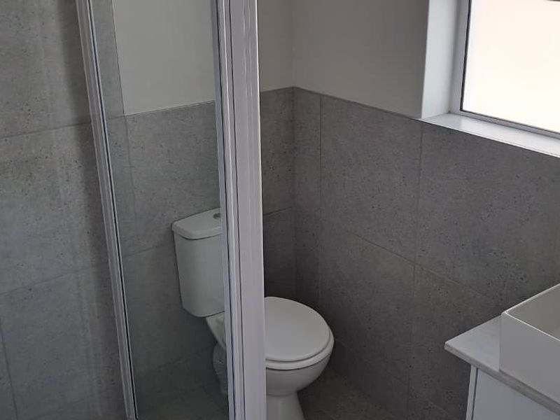 A clean, modern bathroom featuring a shower enclosure, toilet, and a vanity basin with neutral wall tiling.