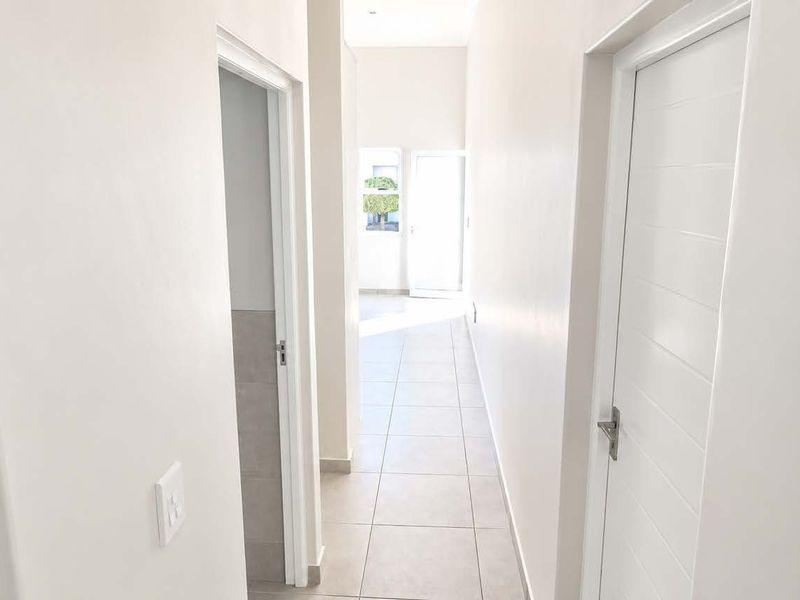 A bright, neutral-toned hallway featuring tiled flooring and multiple internal doors leading to adjacent rooms.