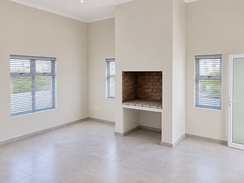 Spacious living area featuring neutral tiled flooring, built-in brick fireplace, and large windows with venetian blinds, offering a bright and clean blank canvas.