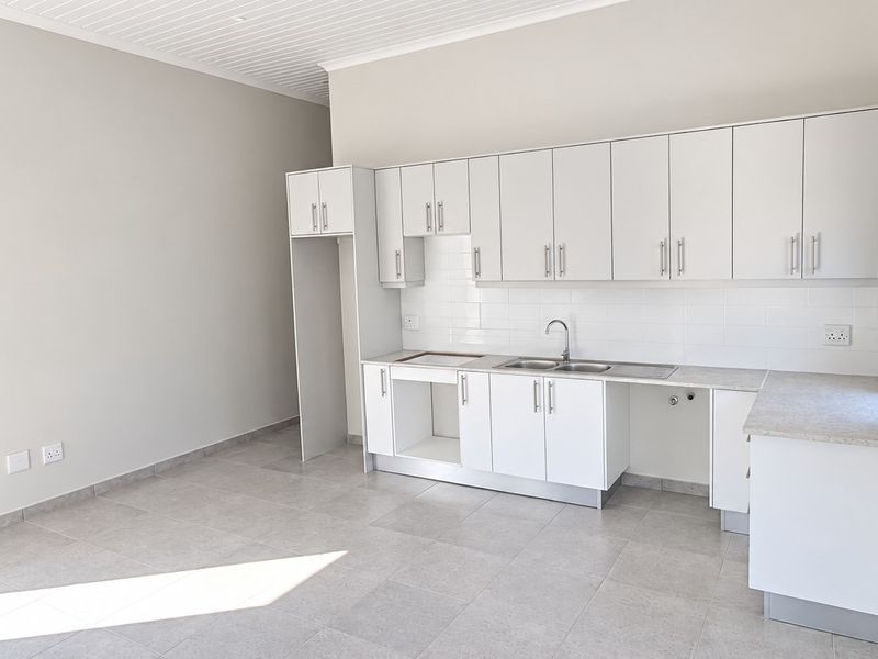 A clean, modern kitchen featuring white cabinetry, a subway tile backsplash, stainless steel sink, and neutral tiled flooring in an open, bright space.