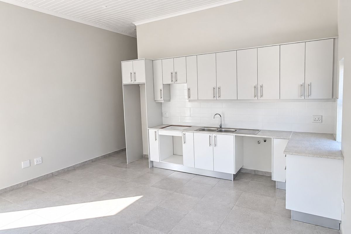 A clean, modern kitchen featuring white cabinetry, a subway tile backsplash, stainless steel sink, and neutral tiled flooring in an open, bright space.