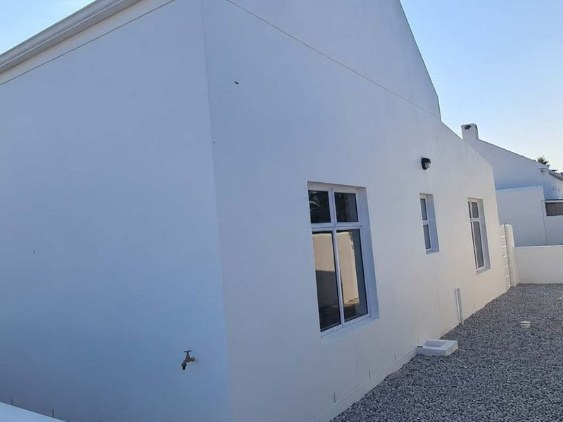 A clean, well-maintained rear exterior view of the house featuring white rendered walls, gravel landscaping, and secure perimeter walling.