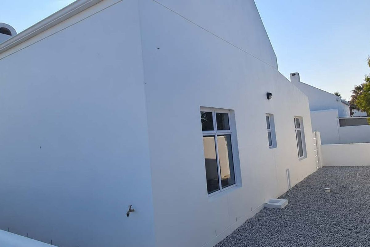 A clean, well-maintained rear exterior view of the house featuring white rendered walls, gravel landscaping, and secure perimeter walling.