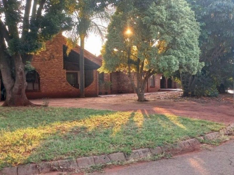A street-facing view of a face brick house featuring arched windows, mature landscaping, and a paved driveway area.