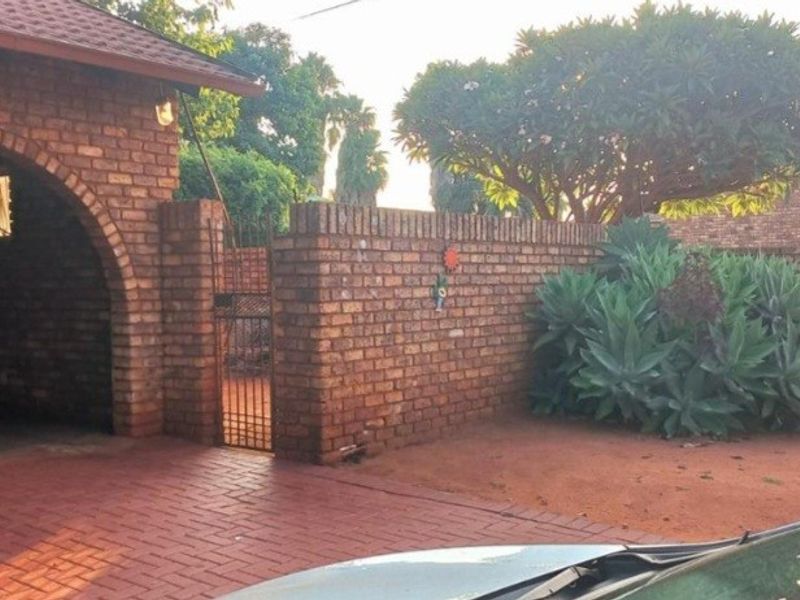 Front exterior view featuring a brick facade, arched carport, paved driveway, and a secure brick boundary wall with a metal gate.